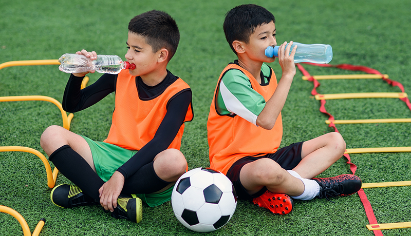 tween boys drinking water on soccer field