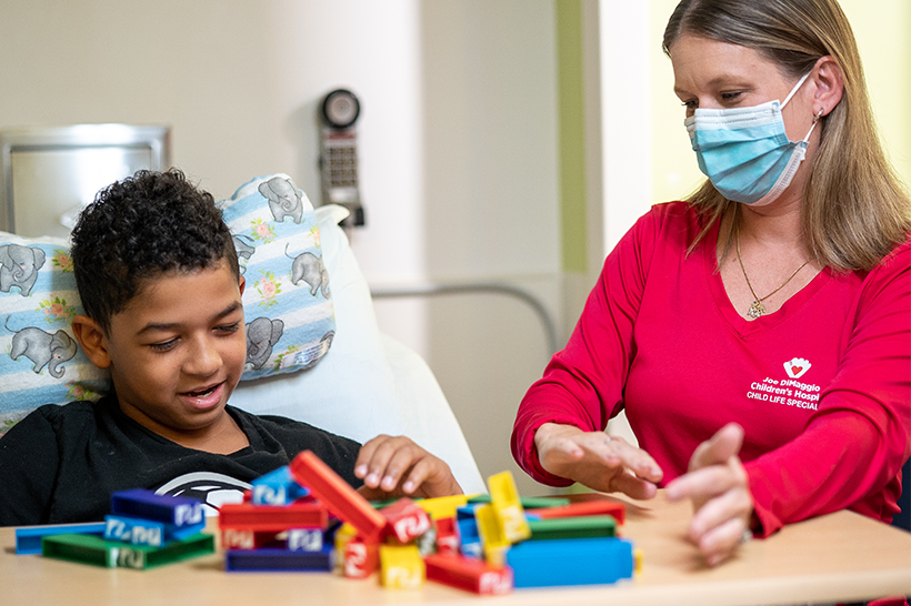 child life specialist playing game with boy in bed